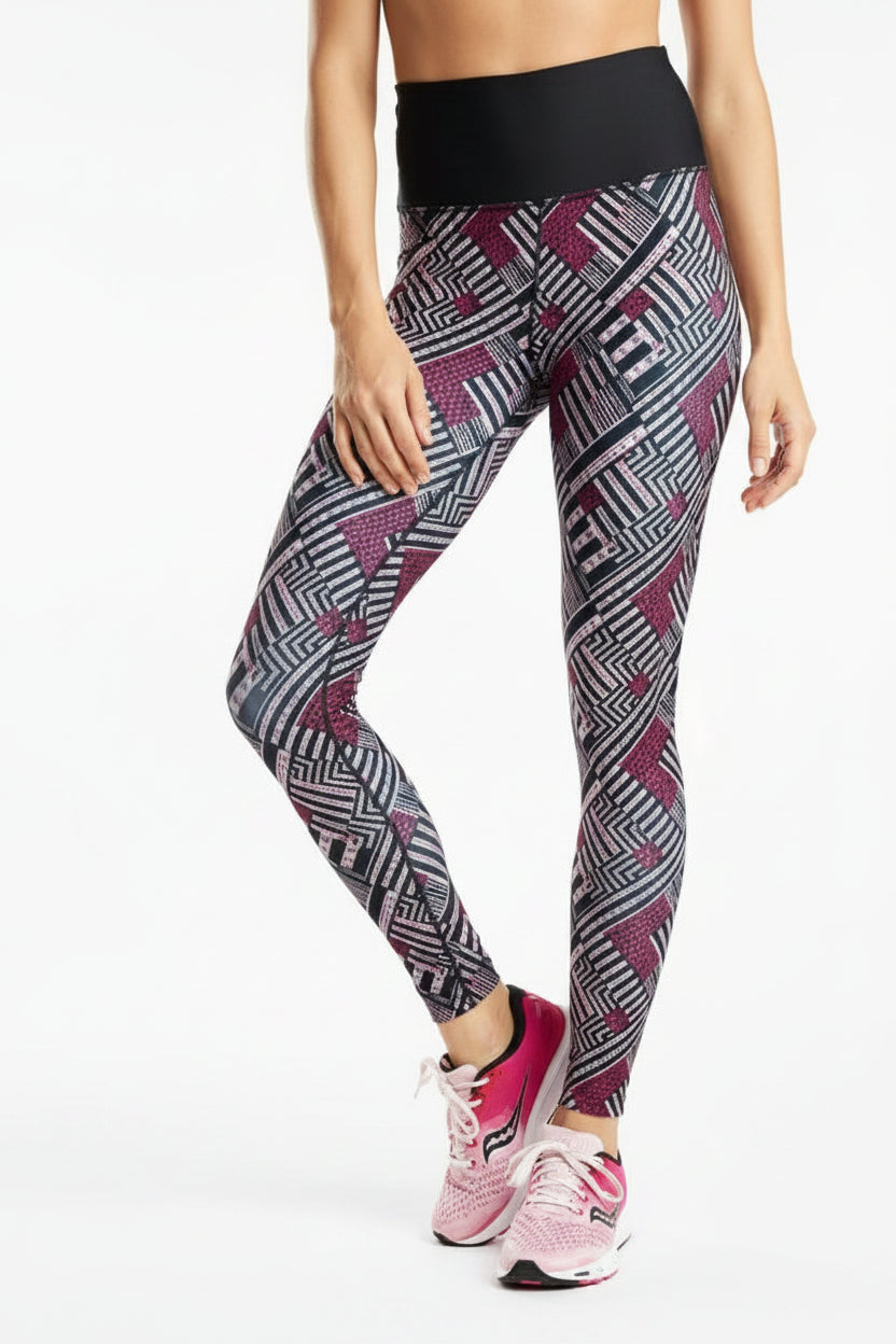 A model wearing high-waisted athletic leggings with a geometric pattern in black, white, and magenta, paired with pink sneakers, against a plain white background.